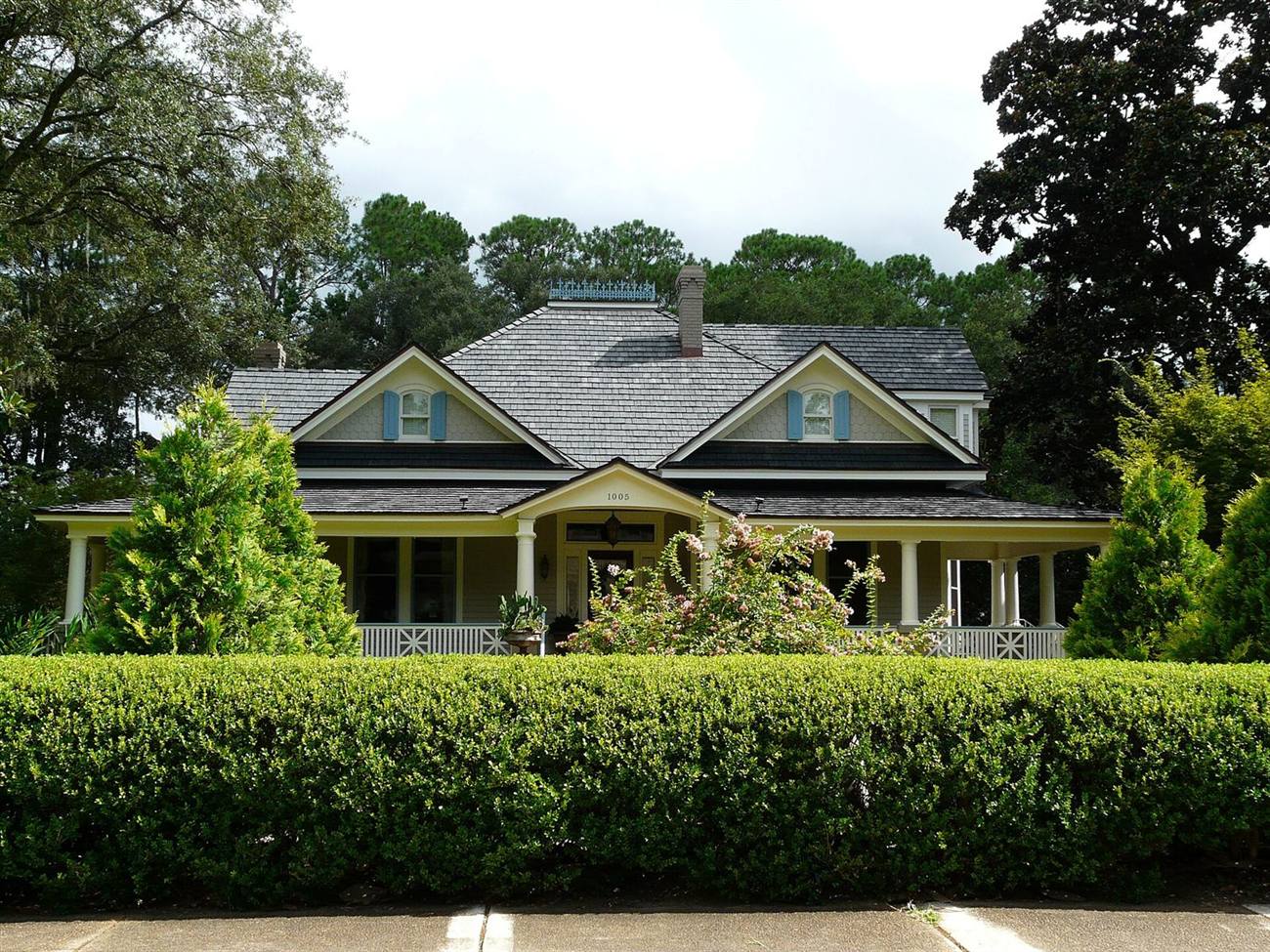 A family home with a wide front porch and a trimmed hedge